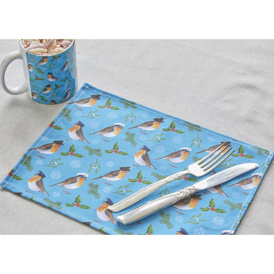 Placemat with our Military Robin Design pattern, mug, and cutlery on a grey tablecloth. Patterned placemat with Robins wearing Military hats of Army, Royal Navy and RAF, with holly and mistletoe and holly on a blue background.