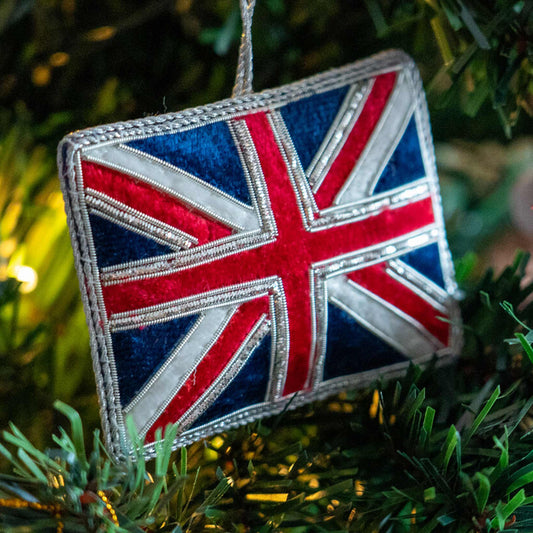 A Union Jack flag-shaped hanging ornament with a silver hanging loop, shown hanging in a Christmas Tree.