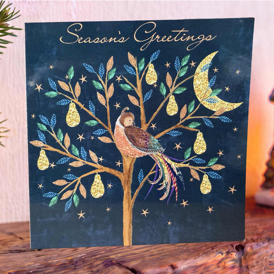 Navy Christmas Card on mantelpiece with a pear tree with gold pears Partridge, stars and crescent moon, topped with gold ‘Season’s Greetings’.