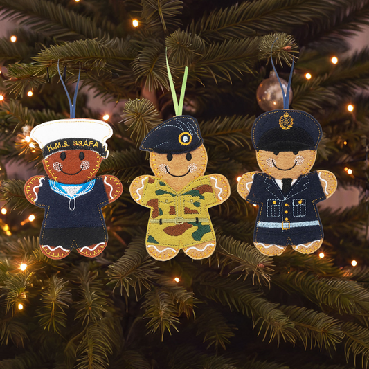 3 gingerbread-style Christmas ornaments of Royal Navy, Army and RAF personnel hanging on a Christmas tree.