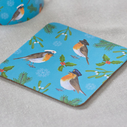 Coaster with military Robin design on a blue background, showing cork back. Patterned coaster with 3 Robins each wearing a hat of the Army, Royal Navy and RAF, with holly and mistletoe and holly on a blue background. On a great table cloth with with a bit of a matching mug shown in top left corner.