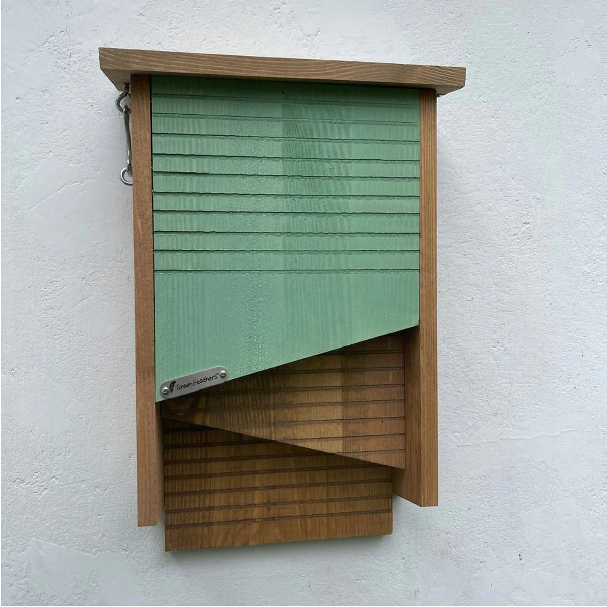 Wooden bat house with green slatted design on a white wall