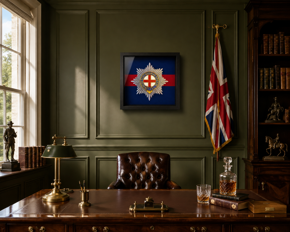 A framed Coldstream Guards insignia displayed on a dark green wall in a vintage, book-filled study with a wooden desk, leather chair, and union flag.