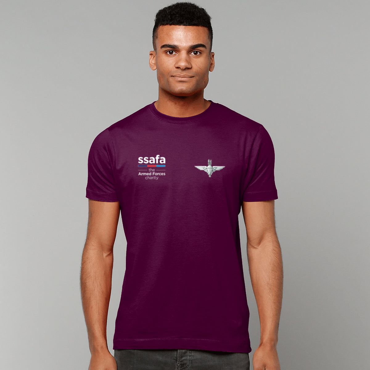 A man wearing a maroon t-shirt showing an MOD licensed Parachute Regiment (King's Crown) insignia to left chest and SSAFA logo to right chest.