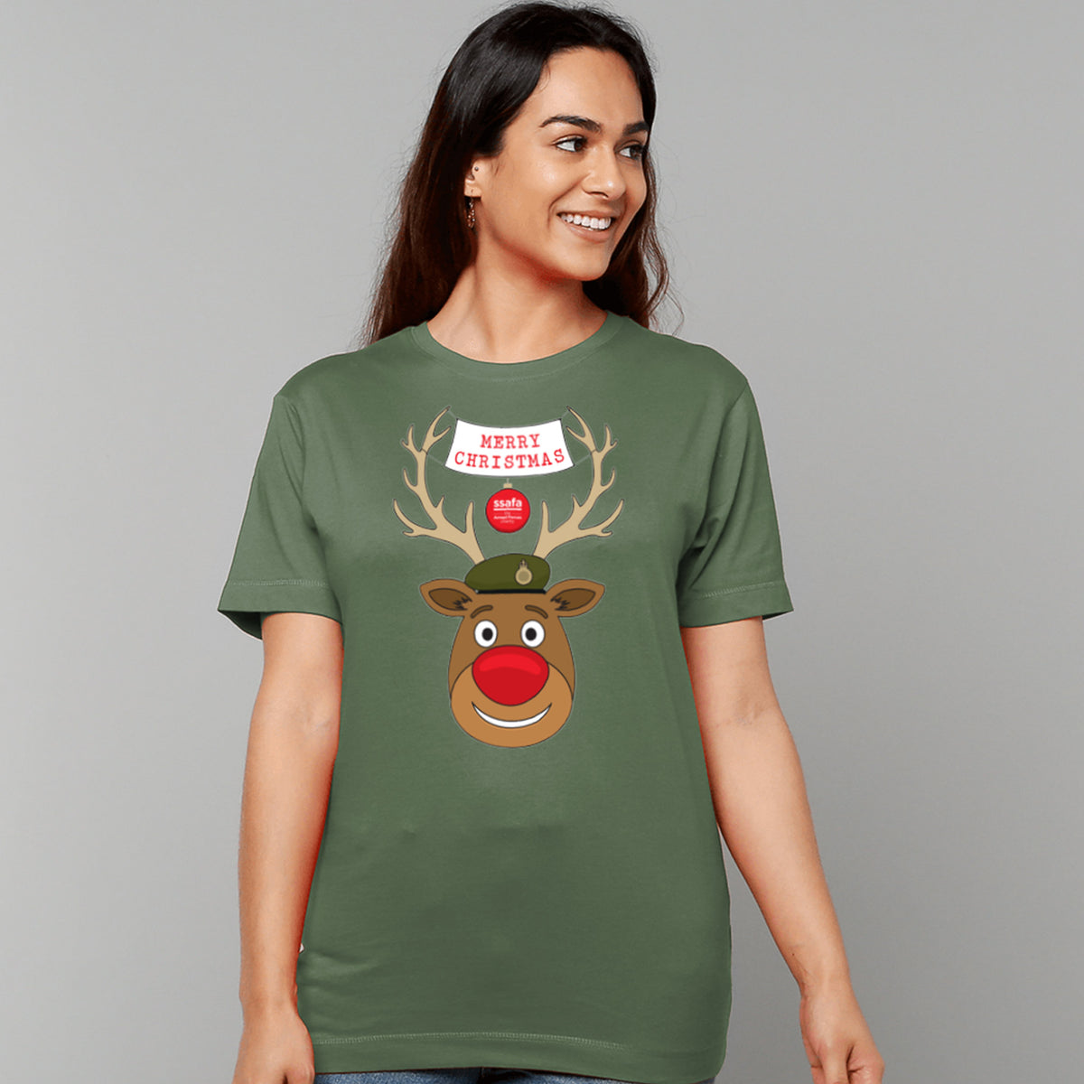 A woman wearing a military green short-sleeve crewneck t-shirt featuring a cartoon graphic of a reindeer with brown antlers, a red nose, an Army hat, and a banner that reads 'MERRY CHRISTMAS'.