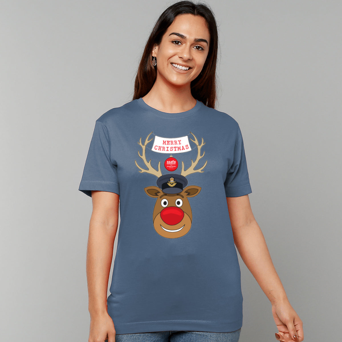 A woman wearing an indigo blue short-sleeve crewneck t-shirt featuring a cartoon graphic of a reindeer with brown antlers, a red nose, wearing a Royal Air Force (RAF) Officer's Peaked Cap. A banner reads 'MERRY CHRISTMAS'.