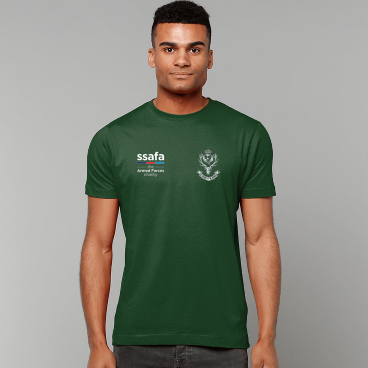 A man wearing a forest green t-shirt showing a MOD licensed Queen's Own Highlanders (Queen's Crown) insignia to left chest and SSAFA logo to right chest.