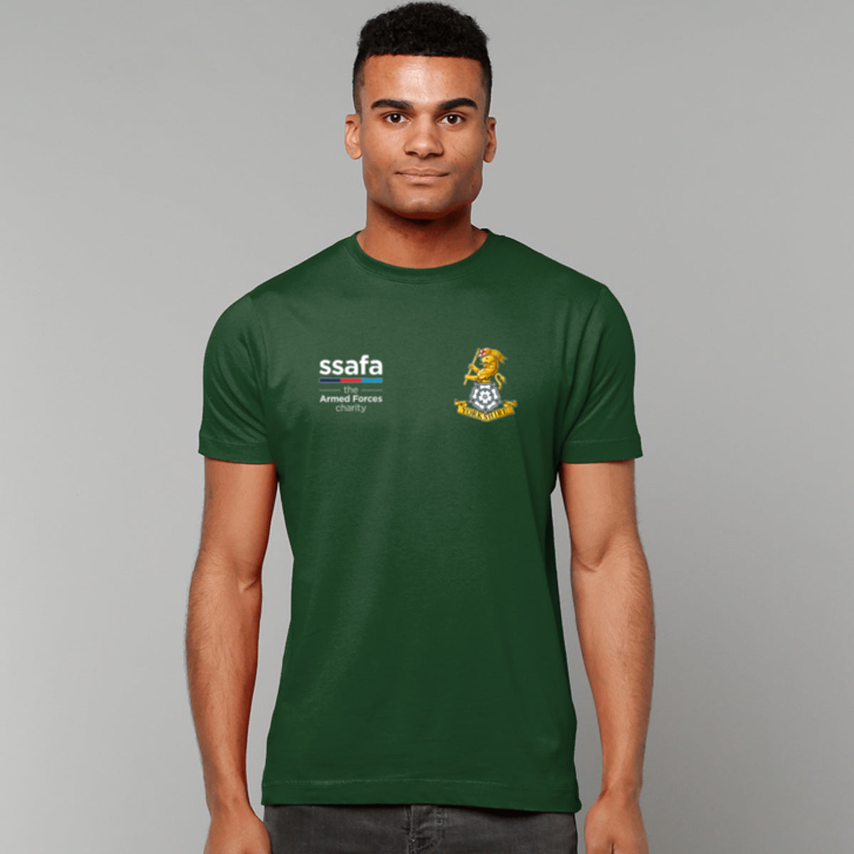 A man wearing forest green t-shirt showing a MOD licensed Yorkshire Regiment insignia to left chest and SSAFA logo to right chest.