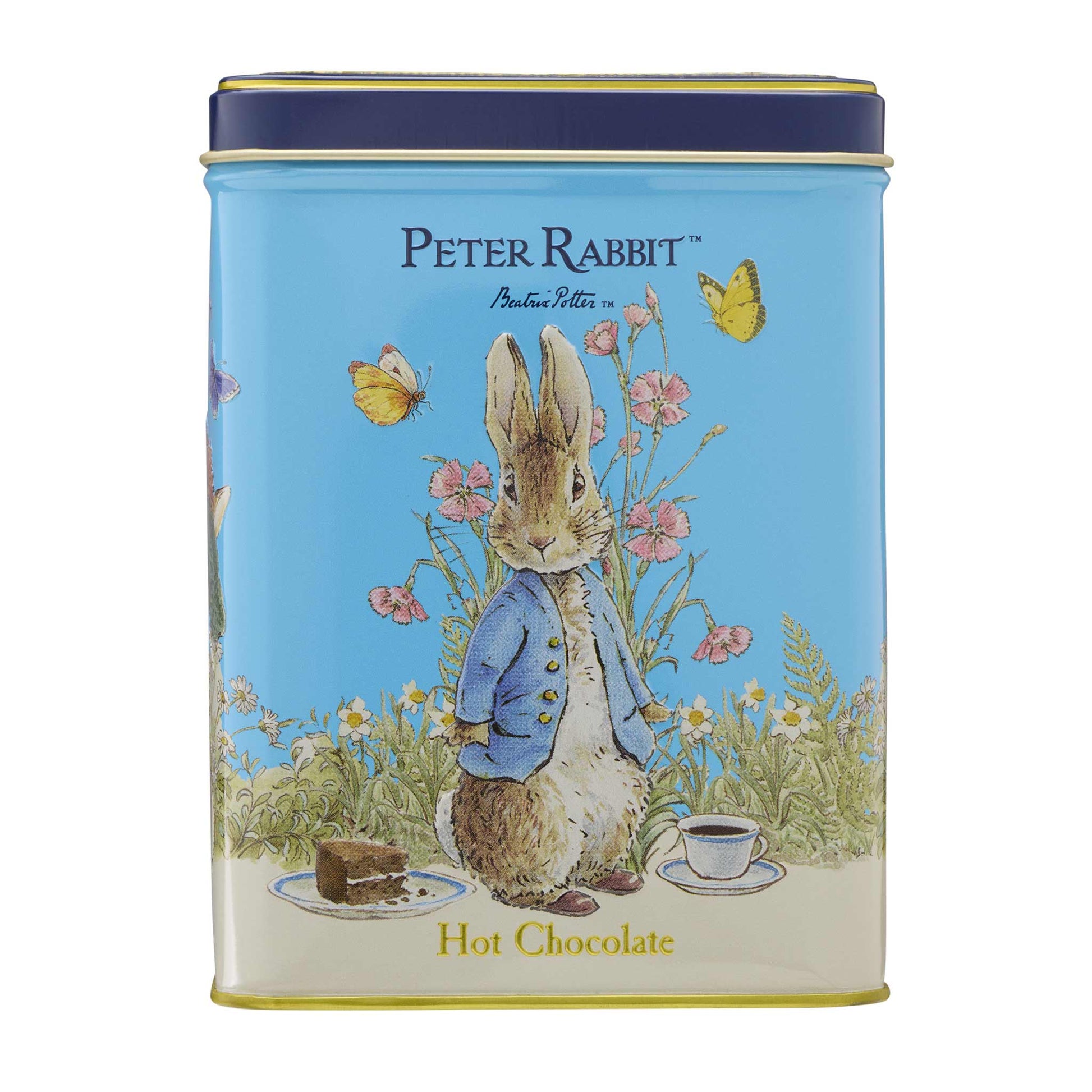 A round metal tin for Peter Rabbit Hot Chocolate featuring a light blue background with an illustration of Peter Rabbit in a blue jacket, surrounded by flowers, butterflies, a chocolate bar, and a cup of hot chocolate. The tin has a dark blue lid and gold trim, with 'PETER RABBIT' and 'Peter Rabbit' printed at the top and 'Hot Chocolate' at the bottom.