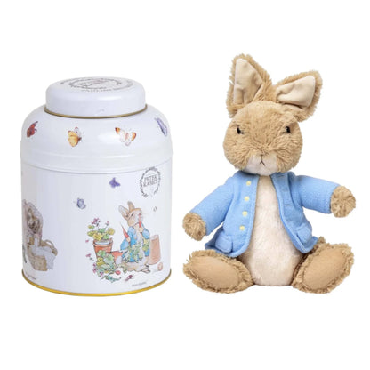 A Peter Rabbit collectible set featuring a plush toy Peter Rabbit in a blue jacket next to a white metal tin decorated with Peter Rabbit illustrations.