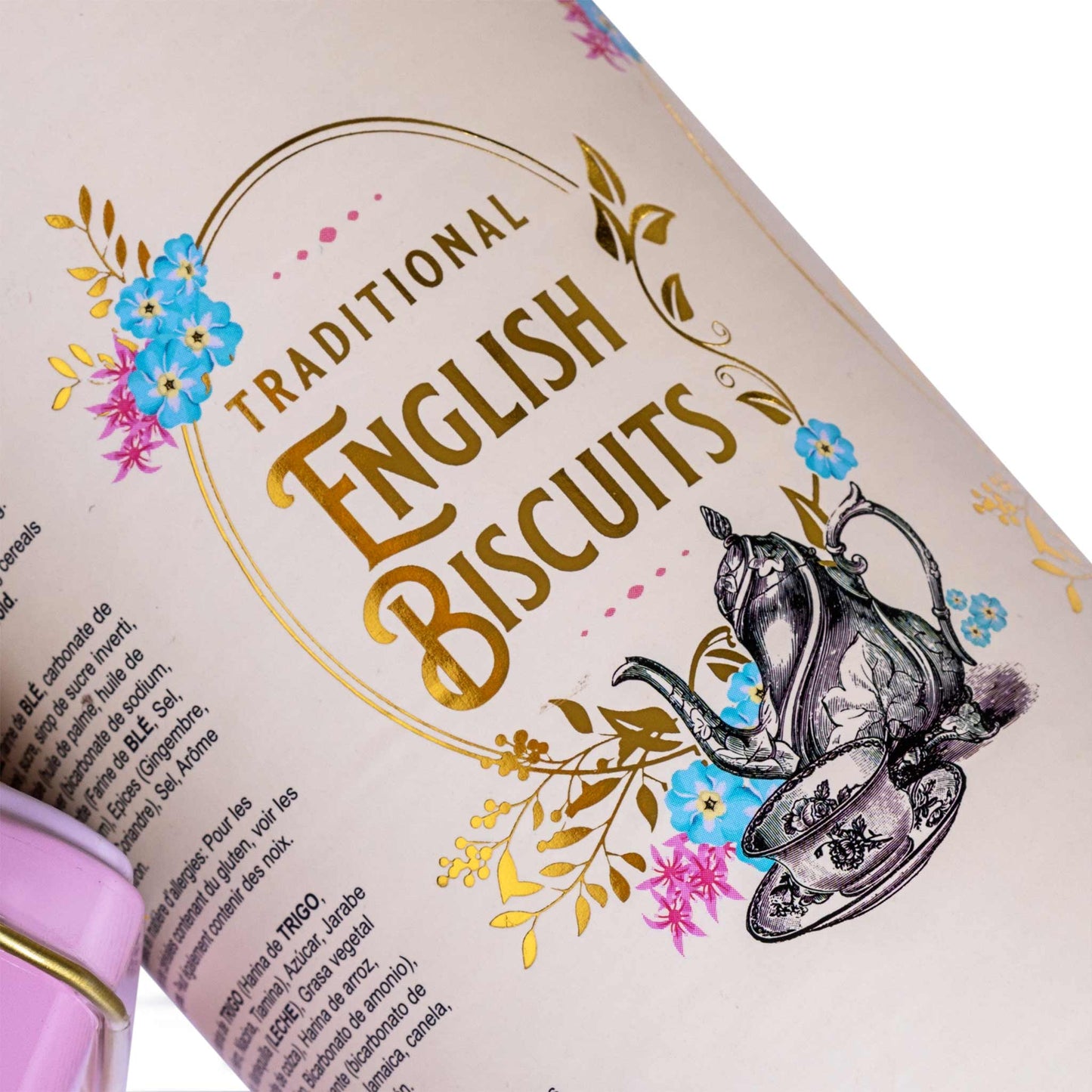 A close-up of a cylindrical tin of Traditional English Biscuits, showing the cream-colored label with gold lettering, blue and pink flowers, and an illustration of a teapot and teacup. The pink tea tin is partially visible at the bottom left.