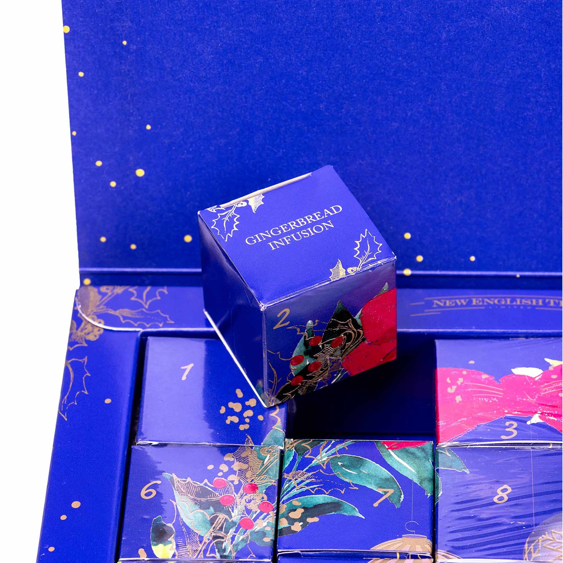 A blue advent calendar box with multiple numbered compartments and one cube-shaped box labeled 'GINGERBREAD INFUSION' standing on top. The packaging features gold details, floral illustrations, and red accents.