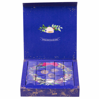 An open royal blue gift box containing six individually boxed tea bags, decorated with gold foil stars and a wreath design on the lid.