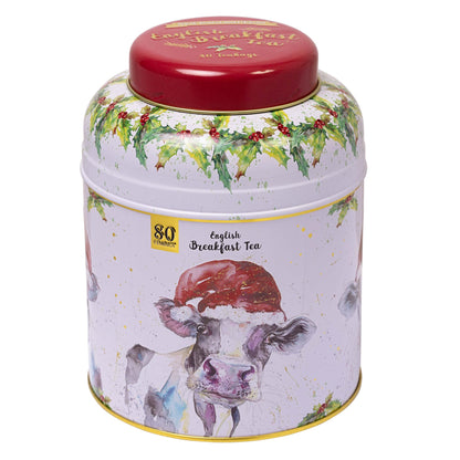 A cylindrical metal tea tin with a red lid and a white body decorated with a watercolor cow wearing a Santa hat, holly garland, and gold accents. The label reads '80 English Breakfast Tea'.