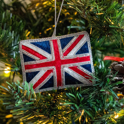 A Union Jack flag-shaped hanging ornament with a silver hanging loop, shown hanging in a Christmas Tree.