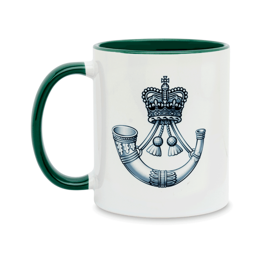 A white ceramic mug with a green handle and interior, featuring a printed insignia of The Rifles on the front. Set against a plain white background.
