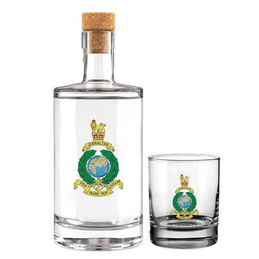 A clear glass bottle with a cork stopper and a matching small clear glass tumbler, both printed with the insignia of the Royal Marines with the Queens Crown, and a gold banner reading 'PER MAR PER TERRAM' moto of the Royal Marines.