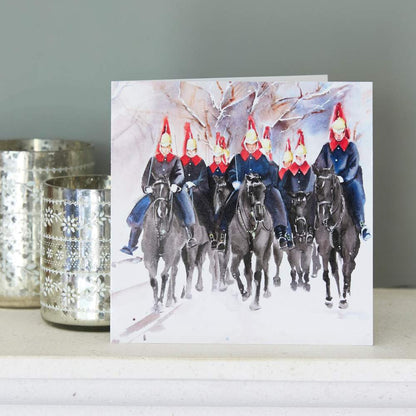Greeting card with a winter scene of the Blues & Royals on horseback wearing red hats, placed against a gryy background.