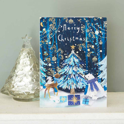 Christmas card with festive design featuring a tree, presents, and animals on a blue background. On a mantel piece.