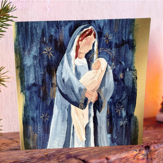 Christmas card on mantelpiece showing a painting of Mary holding baby Jesus against a textured dark blue background with gold stars.