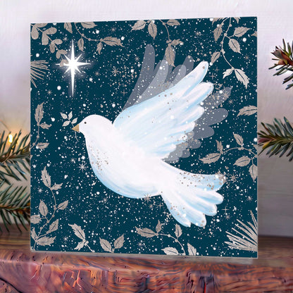 Christmas card on mantelpiece showing a white dove in flight against a starry navy sky, with scattered leaves and a bright star.