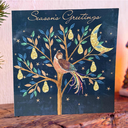 Navy Christmas Card on mantelpiece with a pear tree with gold pears Partridge, stars and crescent moon, topped with gold ‘Season’s Greetings’.