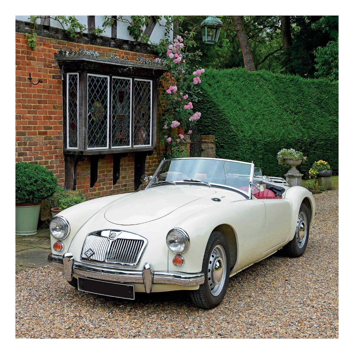 A cream MGA 1600 Roadster from 1959 vintage convertible sports car parked on a gravel driveway in front of a brick house with a bay window and green hedges.