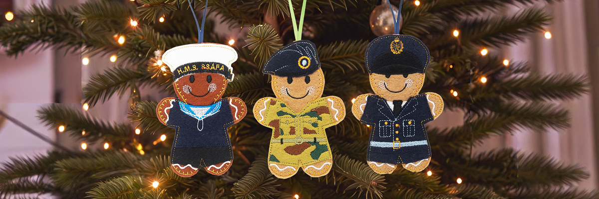 3 gingerbread-style Christmas ornaments of Royal Navy, Army and RAF personnel hanging on a Christmas tree.
