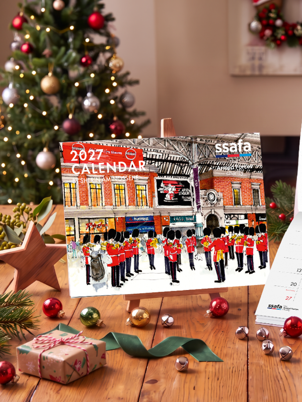 SSAFA Calendar on wooden table with Christmas decorations on table and Christmas tree in the background.