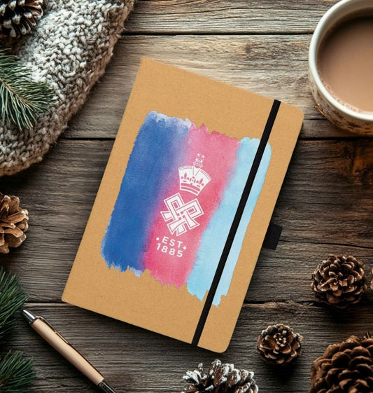Kraft Printed Notebook Front, with tri-stripe watercolur in navy, blue and red, overlaid with the SSAFA crest. Shown on wooden table with Christmas pine cones around.